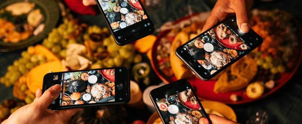 Four people holding smartphones and taking photos of a colorful dinner table full of food