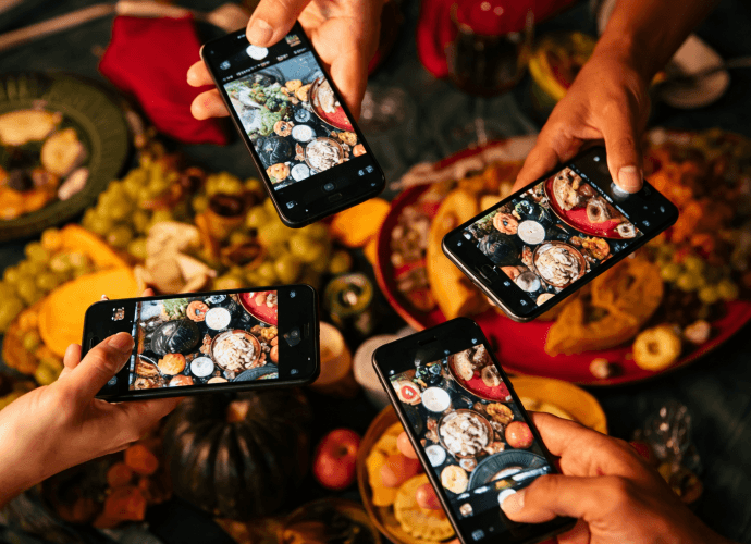 Four people holding smartphones and taking photos of a colorful dinner table full of food