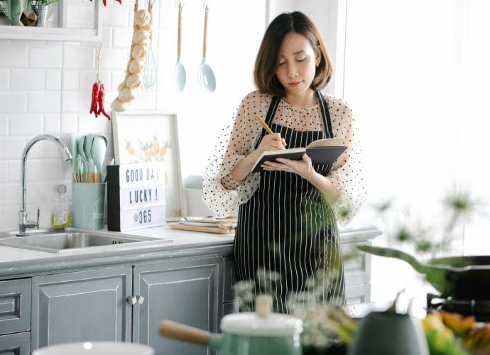 Woman analyzing eating habits after 40 with a notebook and simple healthy food on a calm kitchen table.