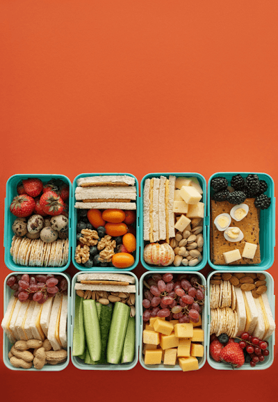 Variety of healthy snacks in colorful meal prep containers on orange background