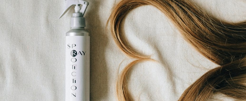 Hair restoration spray bottle next to long healthy blonde hair arranged on a neutral fabric background