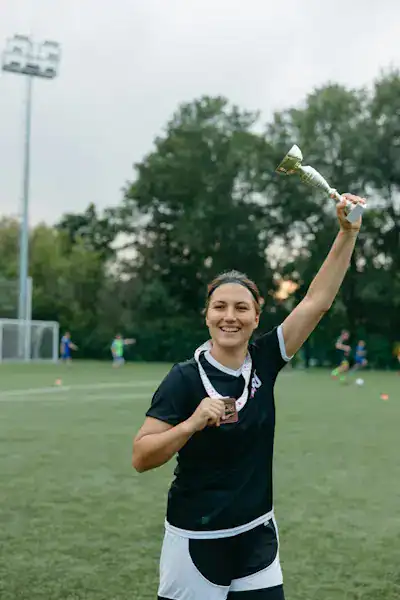 Smiling female athlete holding a trophy on a football field, symbolizing success through delayed gratification and perseverance