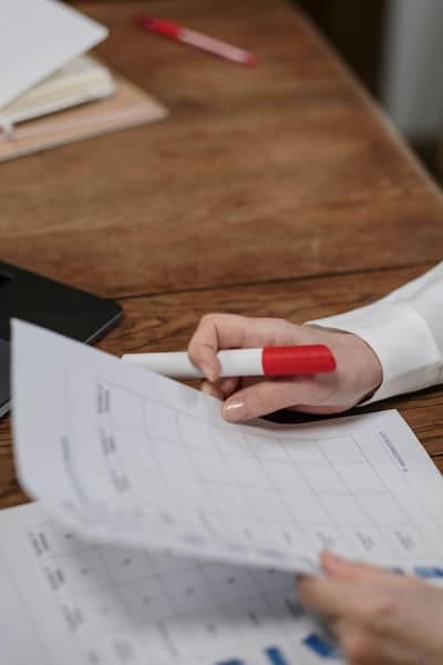 Woman reviewing a progress tracker with a red marker at her desk, symbolizing weekly goal evaluation and personal growth planning.