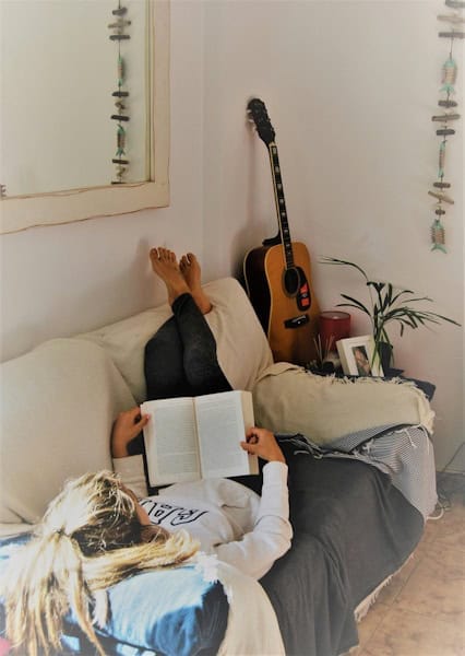 Woman lying on a sofa reading a book in a cozy room with a guitar and home decor, symbolizing introspection and exploring psychological self-awareness for personal growth.