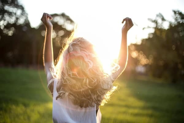 Woman raising arms toward the sun in a field – symbol of inner peace, emotional freedom, and following the feel-good feeling