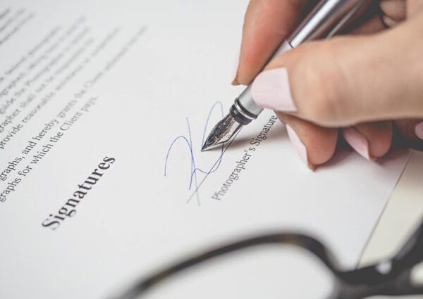 Close-up of a hand signing a document with a silver fountain pen, symbolizing commitment and responsibility.