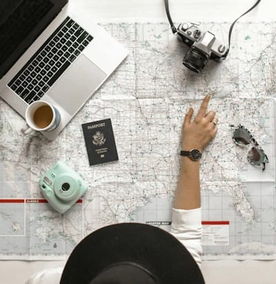 Person planning a trip with a map, camera, and laptop – exploring vacation options within budget as part of the realm of possibility