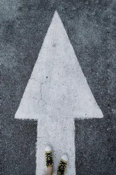 Feet standing on arrow painted on asphalt, symbolizing small steps toward personal growth and life transformation