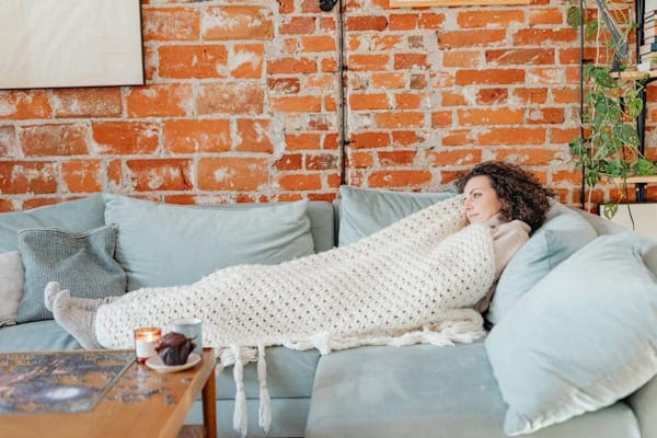 "Woman wrapped in a cozy blanket on a sofa, symbolizing emotional safety and staying inside the comfort zone"