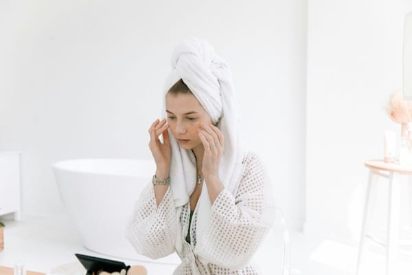 Woman applying skincare cream while wearing bathrobe and towel turban in bathroom