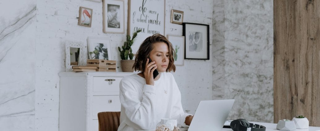 Woman over 40 working from home on a laptop while talking on the phone, representing earning extra money on the side and building financial security.