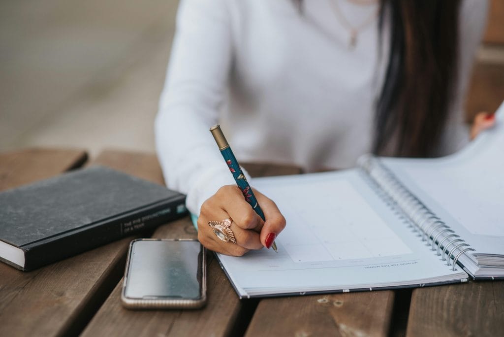 Woman over 40 writing in a planner at a wooden table, representing mindset shift and intentional financial planning.