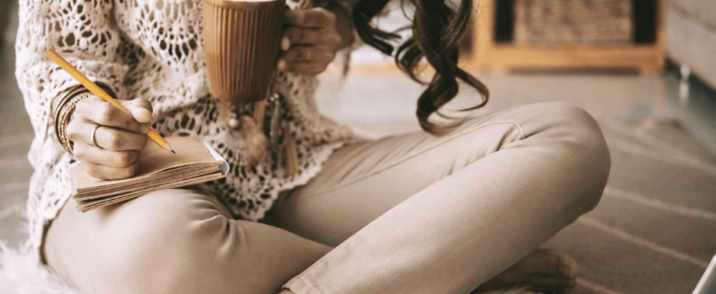Woman in her 40s wearing beige pants, sitting on the floor with a coffee and notebook, calmly reviewing finances after career burnout