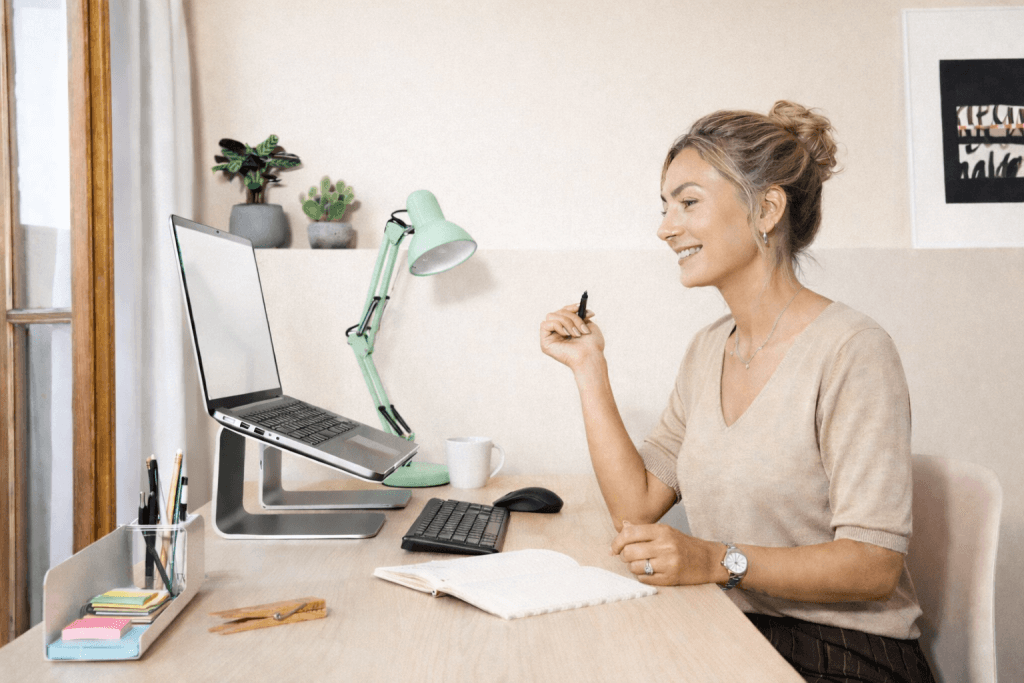 Stylish woman over 40 working from a modern home office desk, building side income on her laptop in a calm, neutral environment.